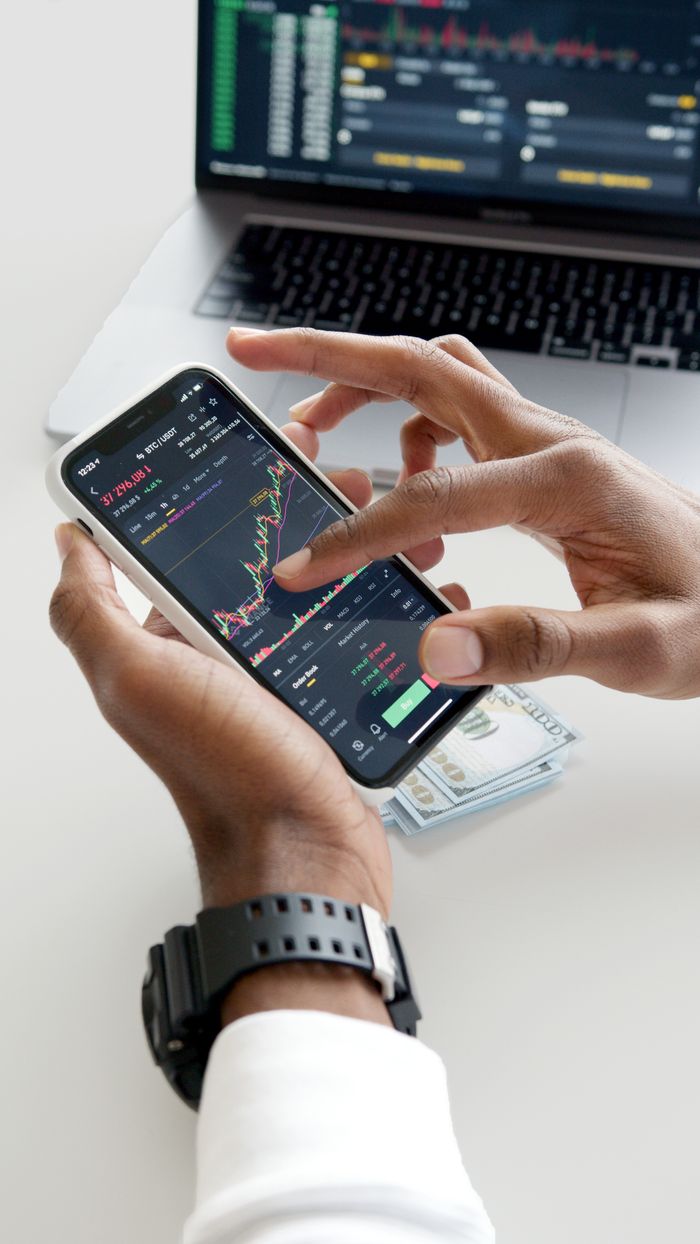 services-01 Hands using smartphone trading app with charts, dollar bills in background.